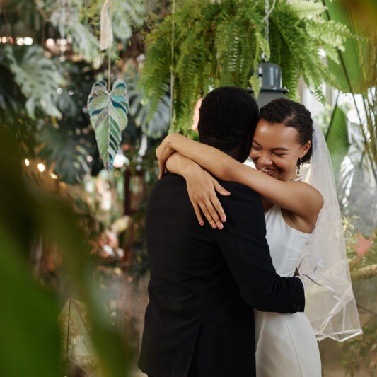 Waist up portrait of young black couple getting married and dancing together in orangerie full of lush tropical plants, copy space